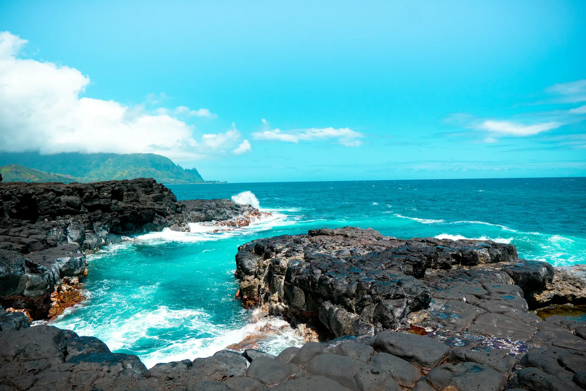 Black lava rock coastline meeting turquoise water in Hawaii