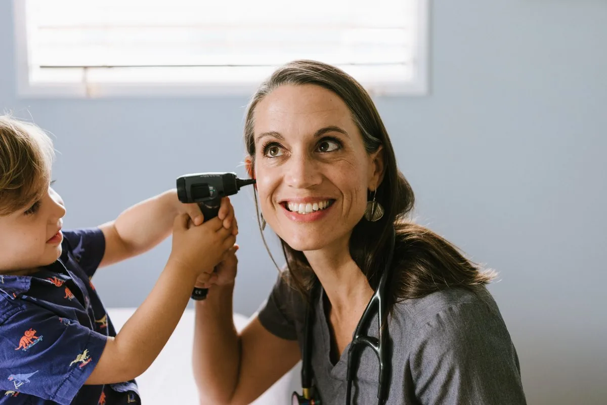 A young patient checks Dr. Corinne De Soto's ear with an otoscope during a family visit at The Koa Clinic